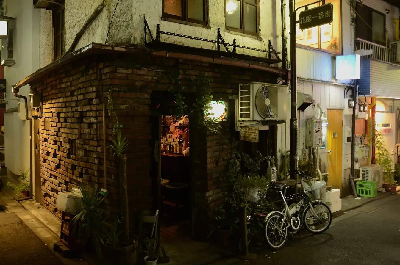 夜晚的新宿Golden Gai一间狭小酒吧，窄门敞向小巷，店内可见摆满酒瓶的吧台