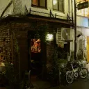 夜晚的新宿Golden Gai一间狭小酒吧，窄门敞向小巷，店内可见摆满酒瓶的吧台