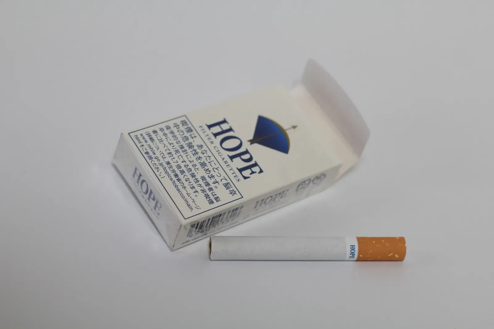 An open pack of Hope, a Japanese short 10-cigarette pack, with one Hope cigarette lying beside it