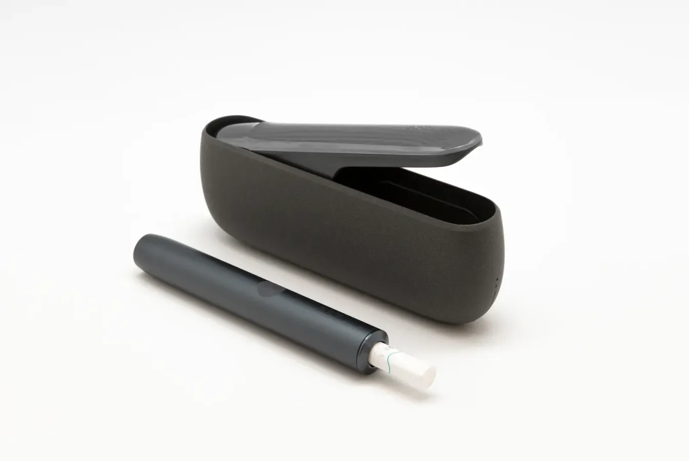 Ein IQOS-ILUMA-Halter mit eingesetztem Tabakstick neben seiner Ladestation