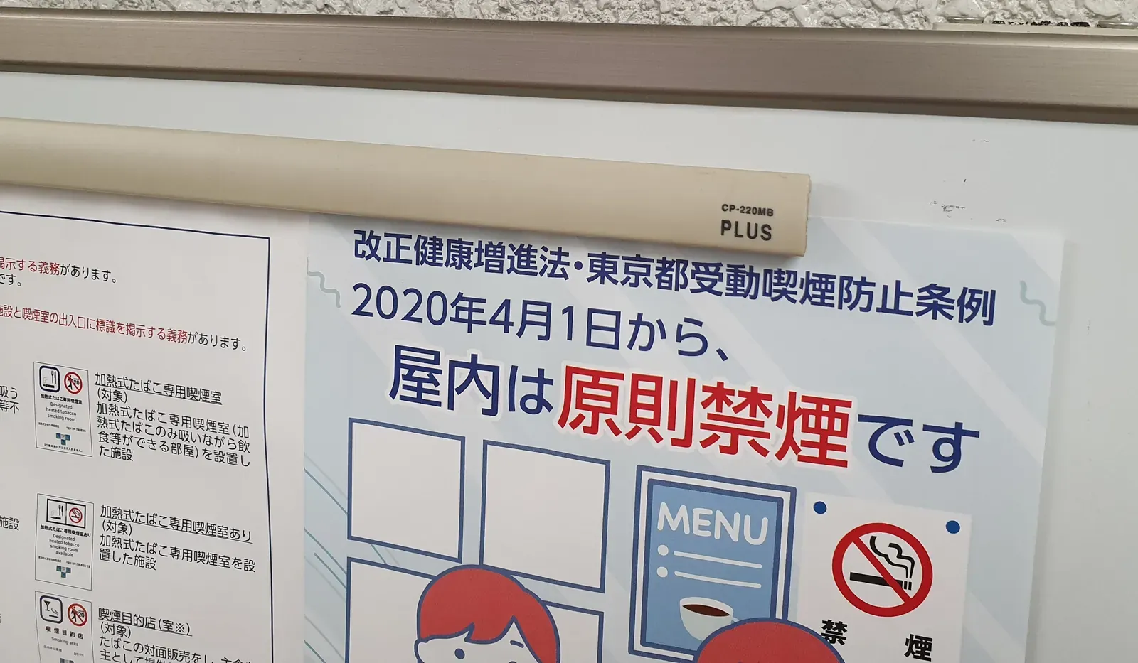 Japanische Hinweistafel mit einem Plakat, das ankündigt, dass Rauchen in Innenräumen ab dem 1. April 2020 grundsätzlich verboten ist; daneben ein Blatt mit den offiziellen Schildern, die Betriebe zeigen müssen, einschließlich des Schilds „ausgewiesener Raucherbereich“ für erhitzten Tabak