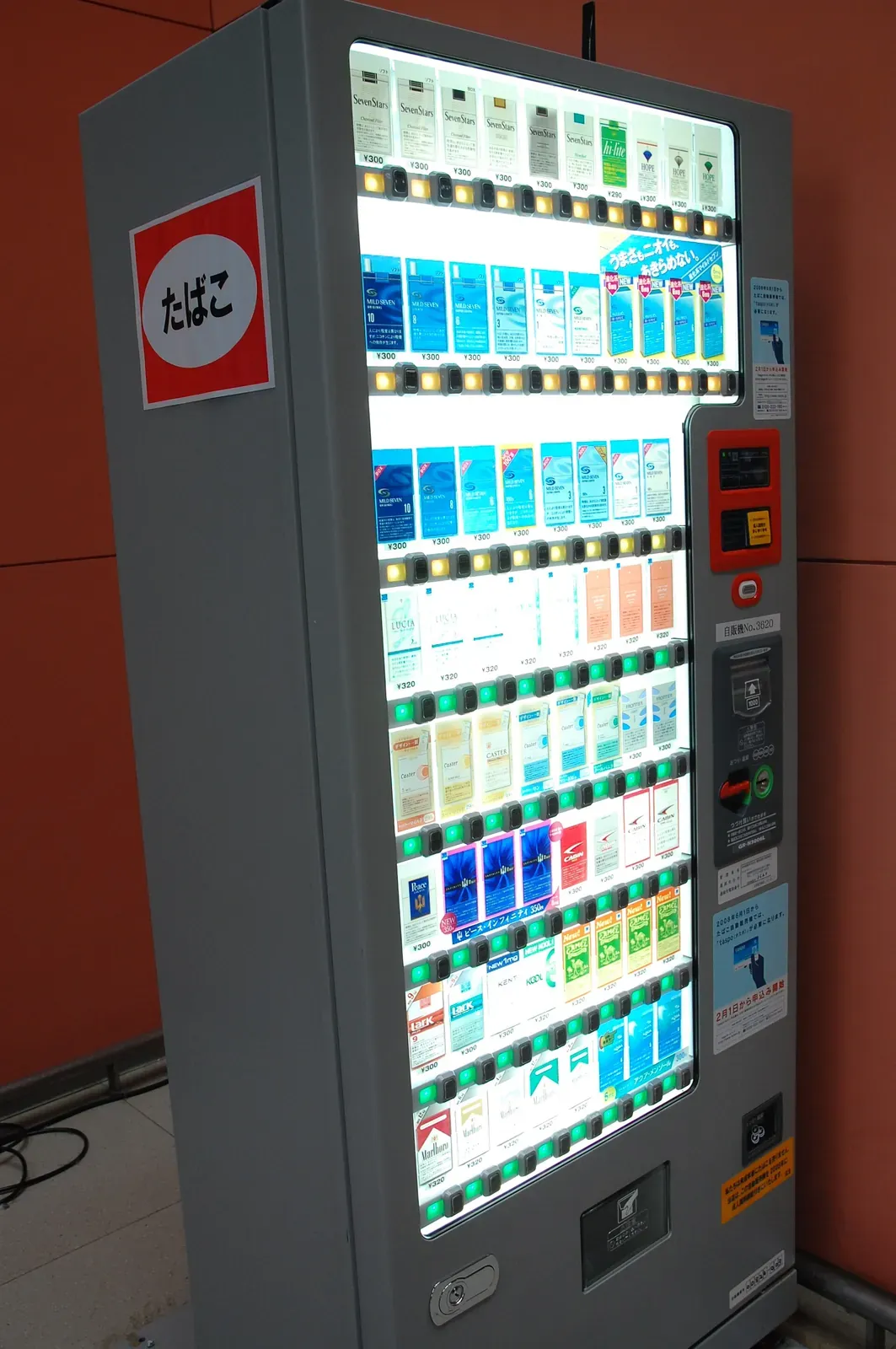 Ein beleuchteter Zigarettenautomat auf einer japanischen Straße; an der Seitenverkleidung hängt noch ein alter Hinweis zur Anmeldung für taspo.
