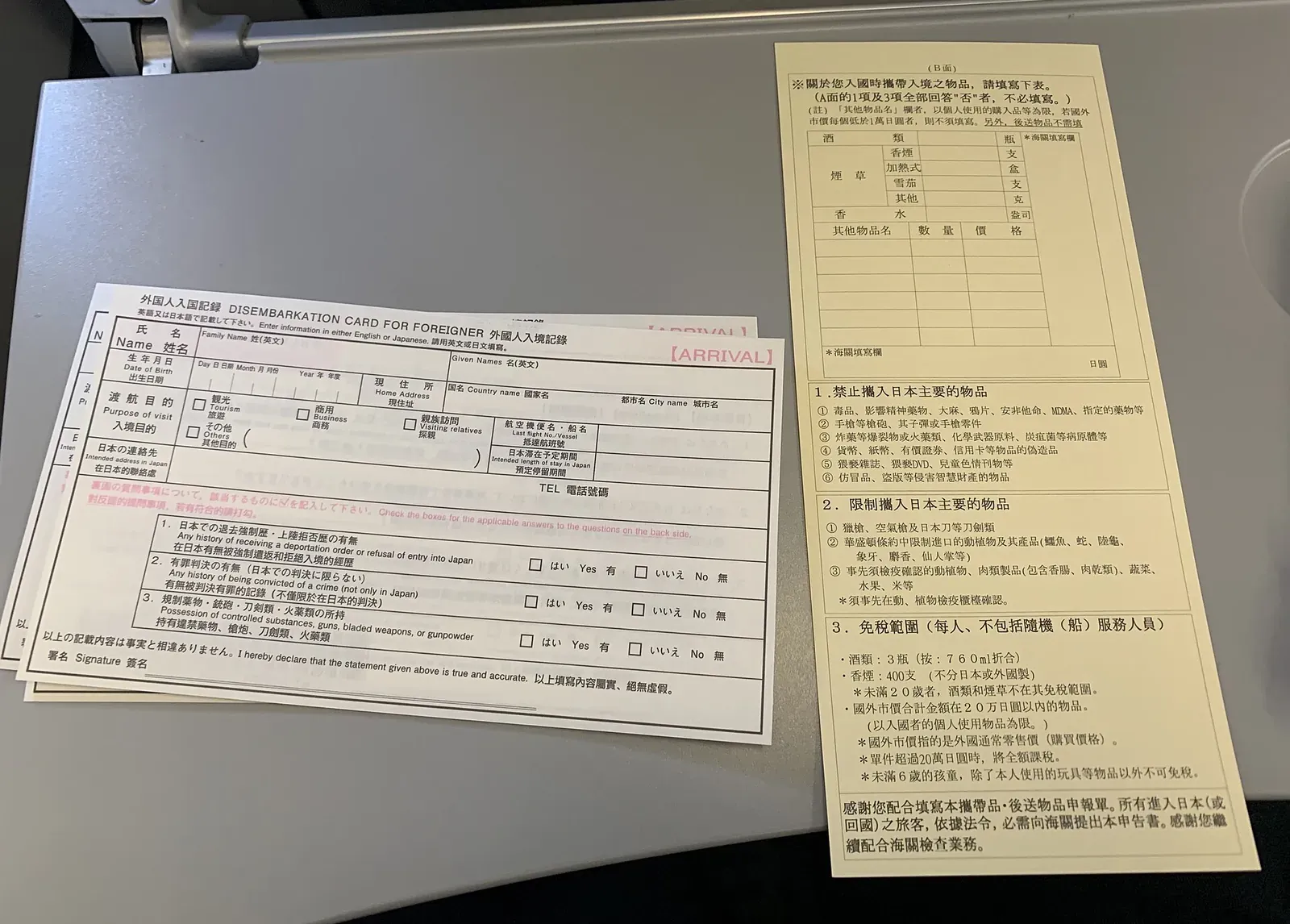 Eine leere japanische Zollerklärung neben Einreisekarten; im Tabakabschnitt stehen getrennte Zeilen für Zigaretten, erhitzter Tabak, Zigarren und sonstigen Tabak