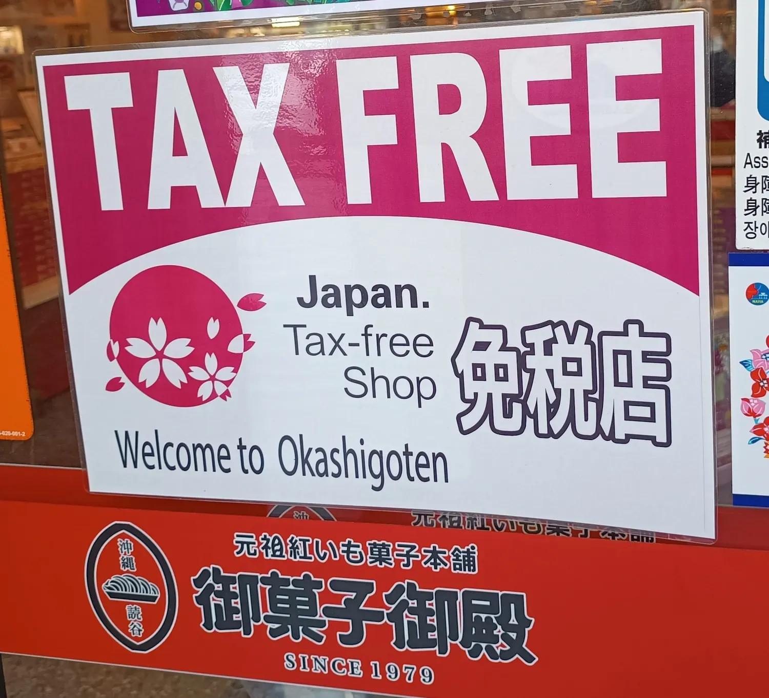 Rosa TAX-FREE-Schild mit dem offiziellen Kirschblütenzeichen von Japan Tax-free Shop und den Worten 免税店 im Schaufenster eines japanischen Geschäfts in der Stadt