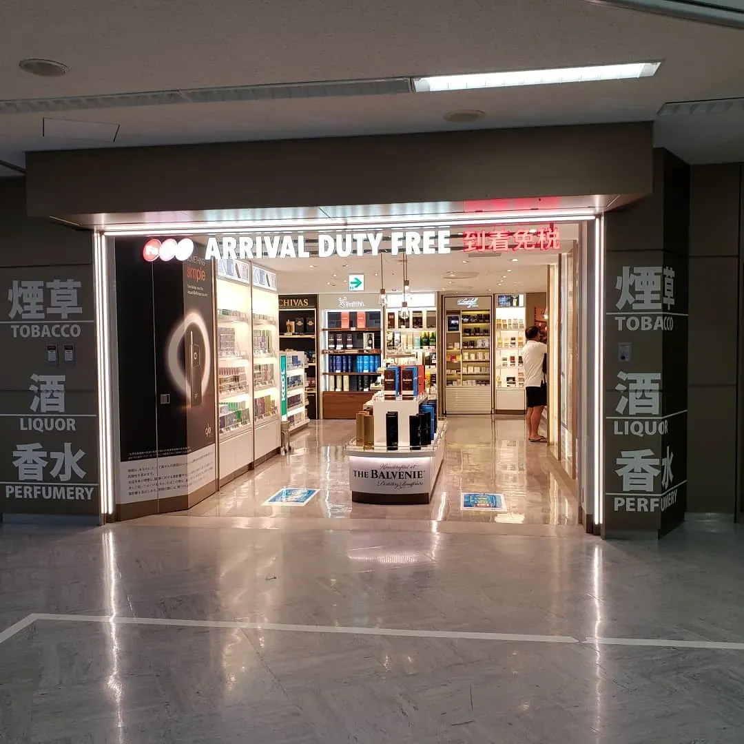 Arrival duty-free shop at Narita Airport, its entrance marked 到着免税 with signs for 煙草 tobacco, 酒 liquor and 香水 perfumery