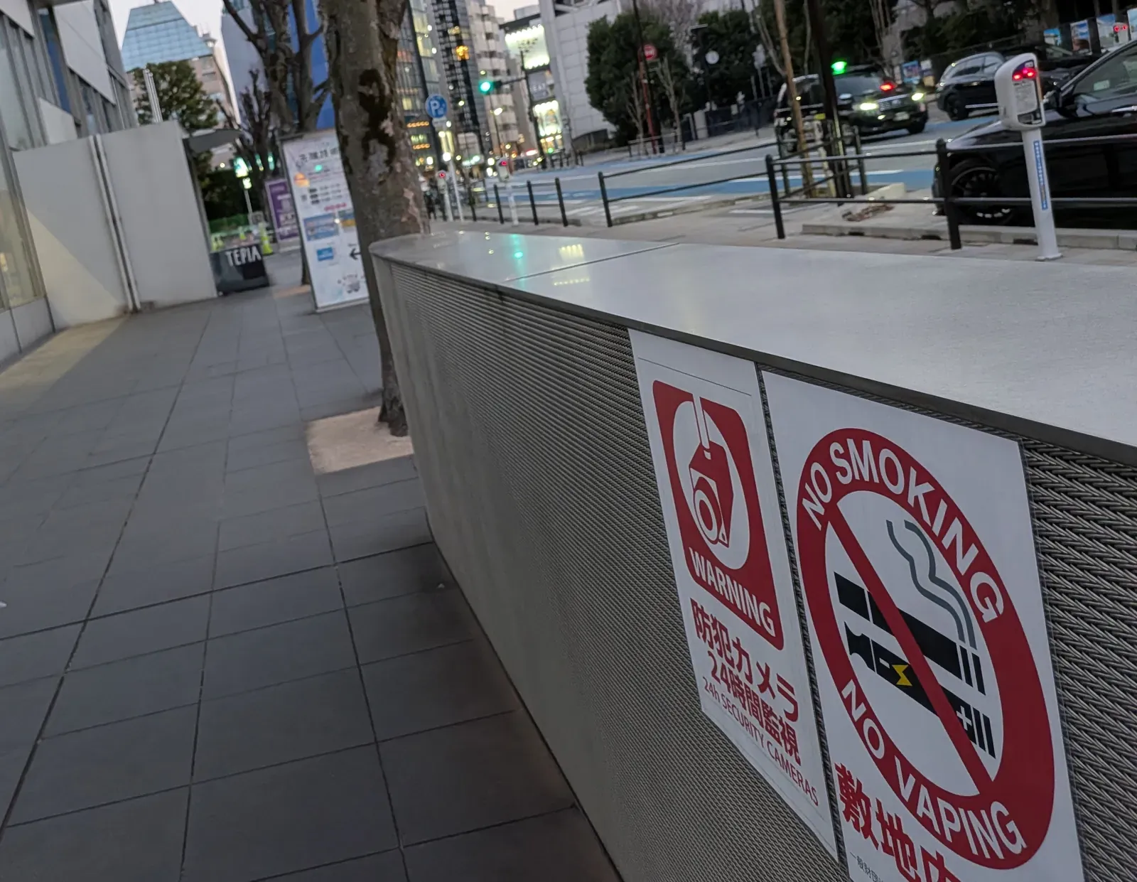 Bilingual NO SMOKING / NO VAPING sign on a street-side wall in Tokyo, banning both cigarettes and vapes on the premises