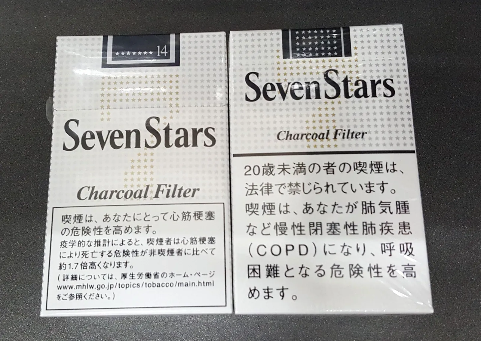 Two Seven Stars Charcoal Filter cigarette packs from Japan side by side, showing the Japanese health warning text