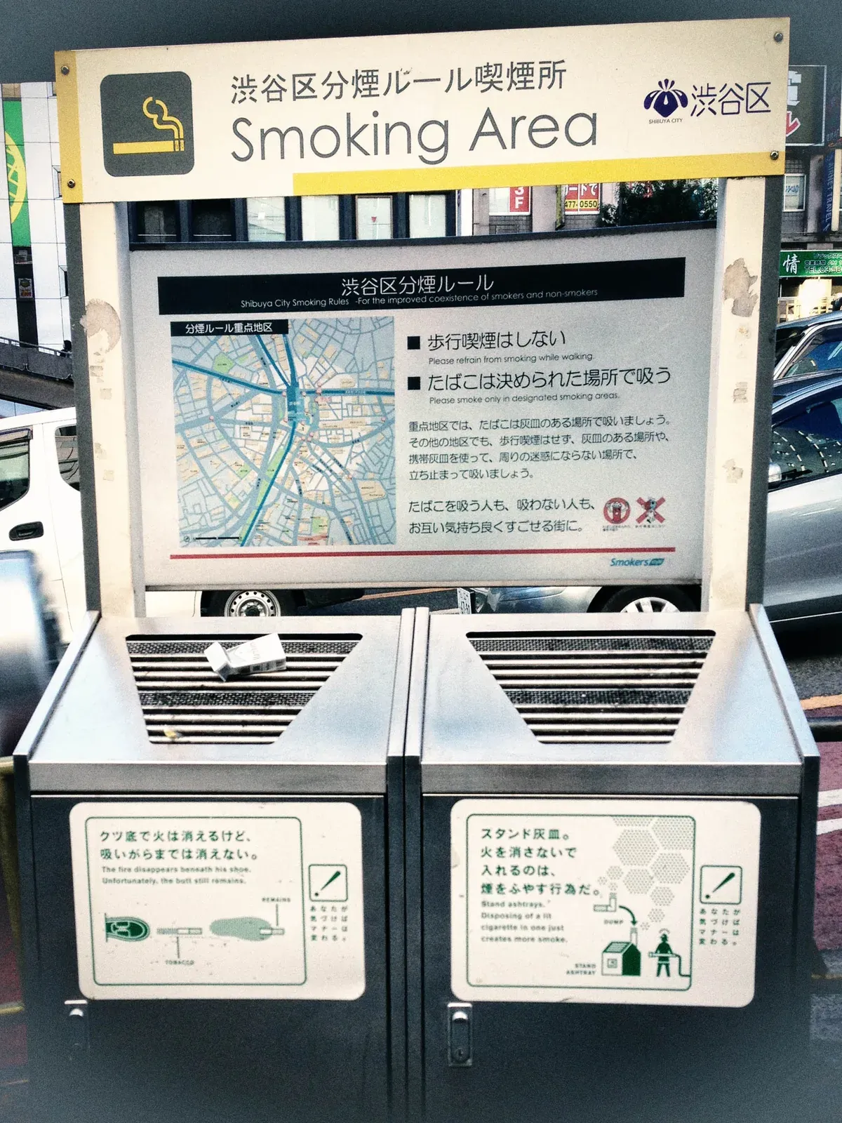 Shibuya City designated smoking area with a Smoking Area sign board, a posted map of the ward smoking rules, and two stand ashtrays