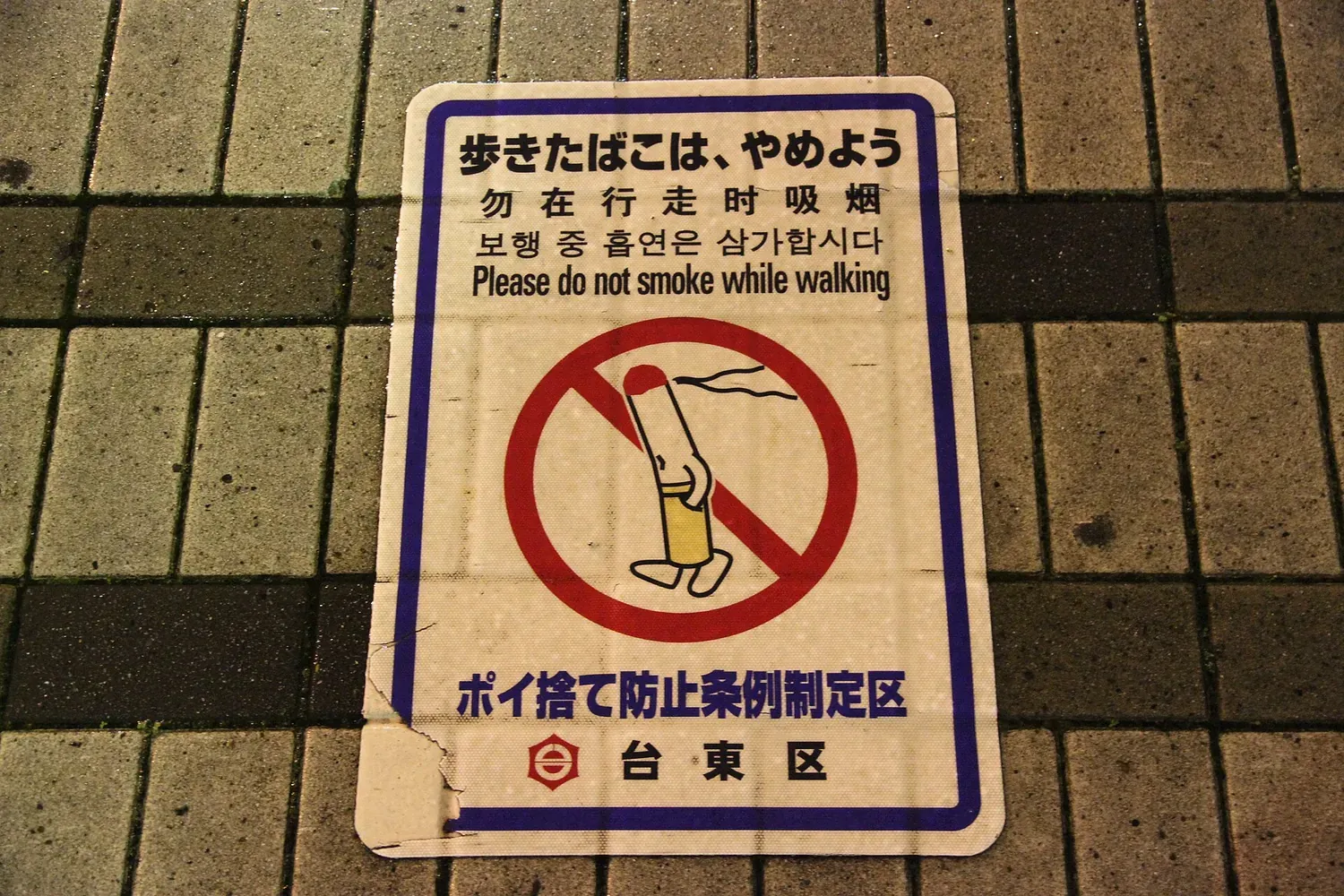 Aufkleber auf dem Gehweg im Bezirk Taito auf Pflastersteinen in Tokio mit der Aufschrift „Bitte rauchen Sie nicht beim Gehen“ auf Japanisch, Chinesisch, Koreanisch und Englisch sowie einer durchgestrichenen brennenden Zigarette