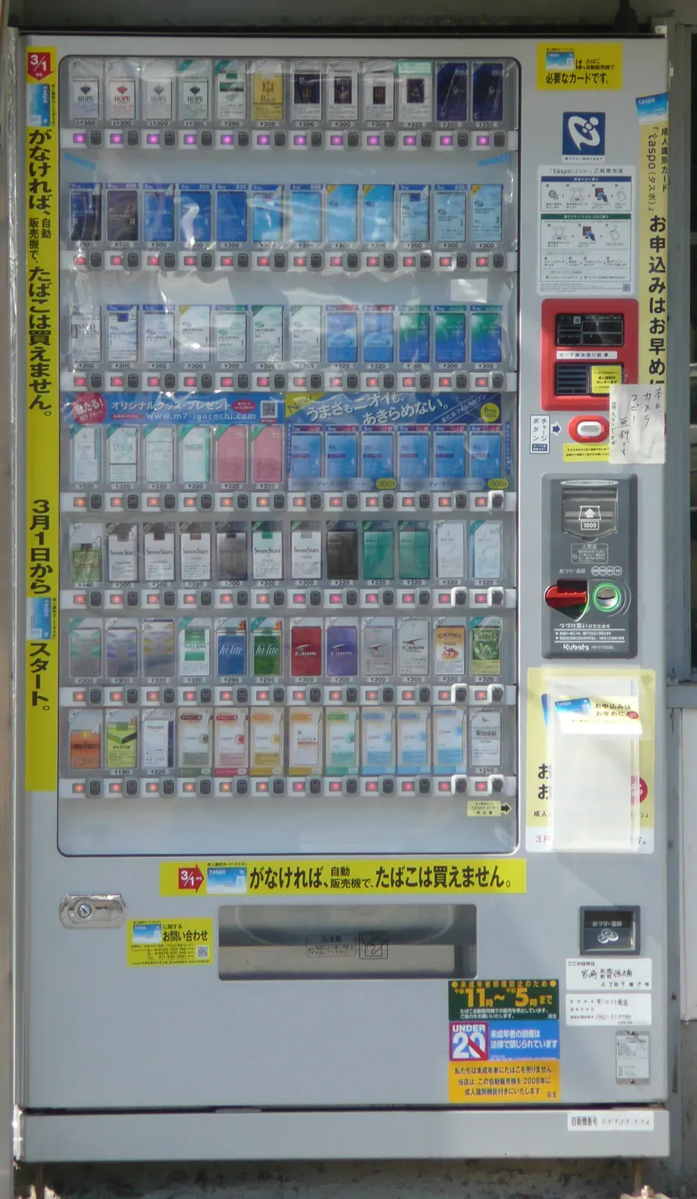 一台日本香烟自动售货机,右侧配有 taspo 年龄验证读卡器,并贴有写着“UNDER 20”的警示贴纸,说明未成年人吸烟受法律禁止