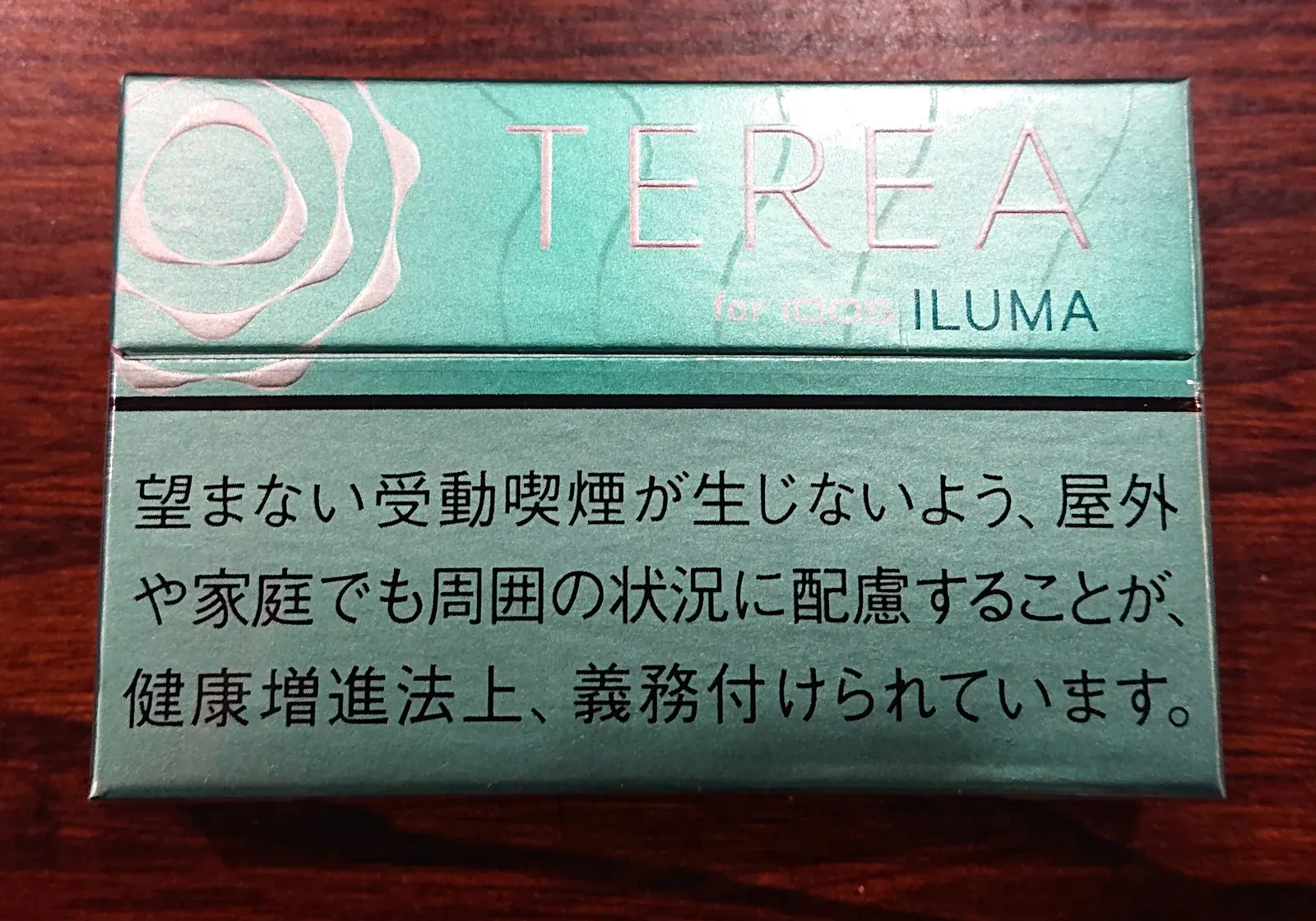 Eine TEREA-Packung für IQOS ILUMA auf einem Holztisch; sichtbar ist der aufgedruckte japanische Gesundheitshinweis