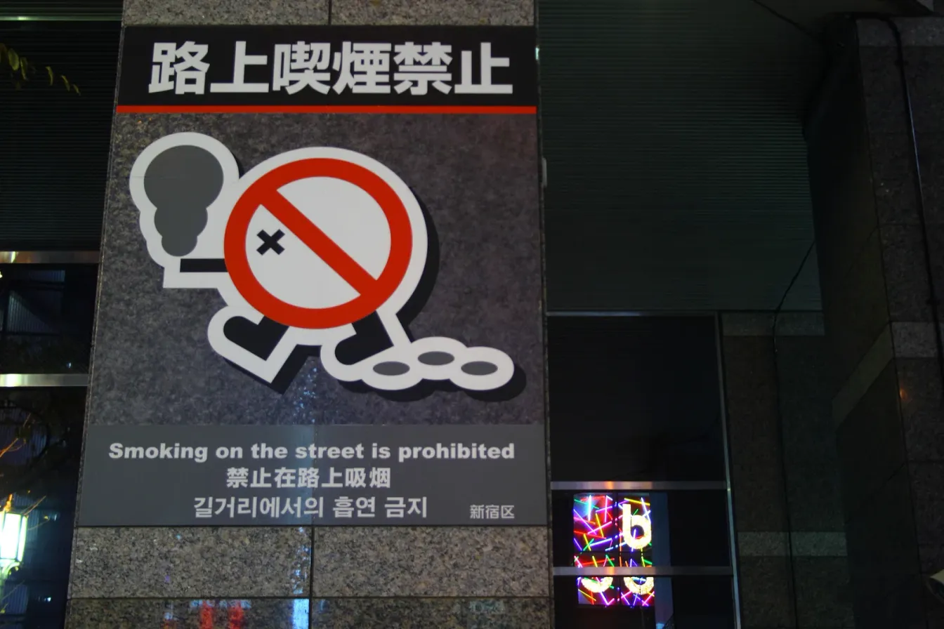 Straßenschild im Bezirk Shinjuku mit der Aufschrift 路上喫煙禁止, einer durchgestrichenen Zigarette und dem englischen Text „Smoking on the street is prohibited“