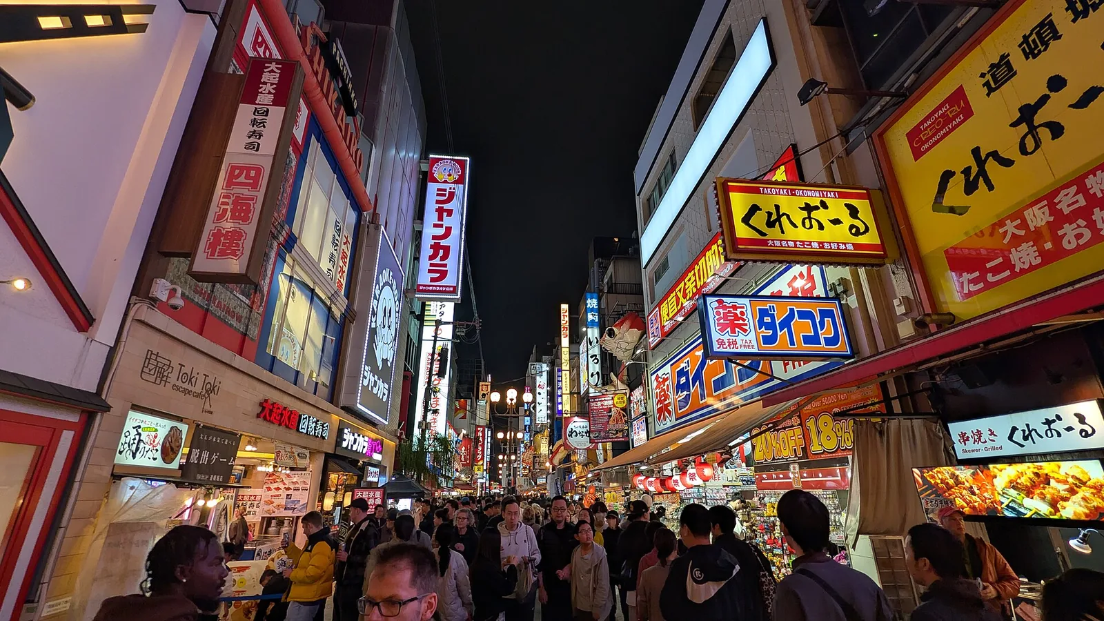 A narrow Dōtonbori street at night, walled on both sides with illuminated restaurant signs and neon lettering