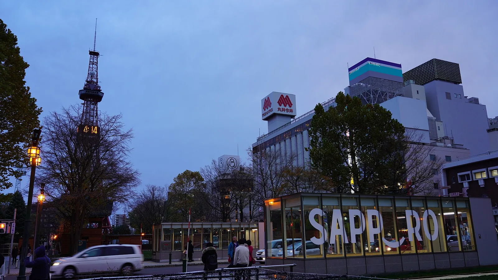 Sapporo TV Tower lit at dusk above Ōdōri Park, with the illuminated SAPPORO sign along the street below