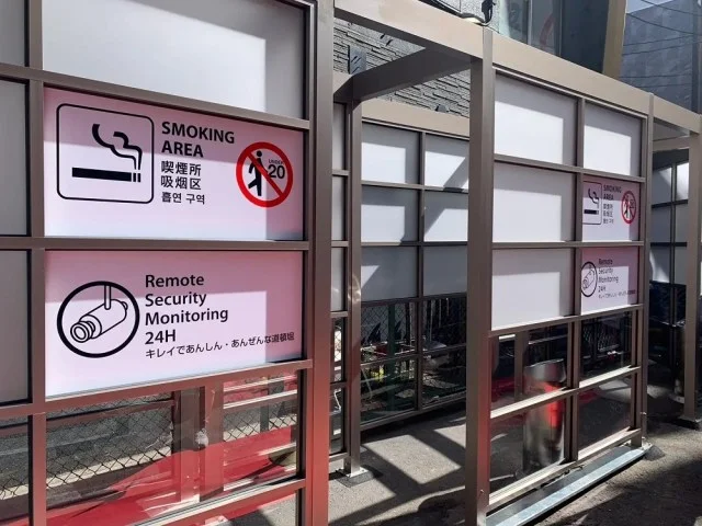 Public outdoor smoking shelter in Tokyo — glass partitions and official signage