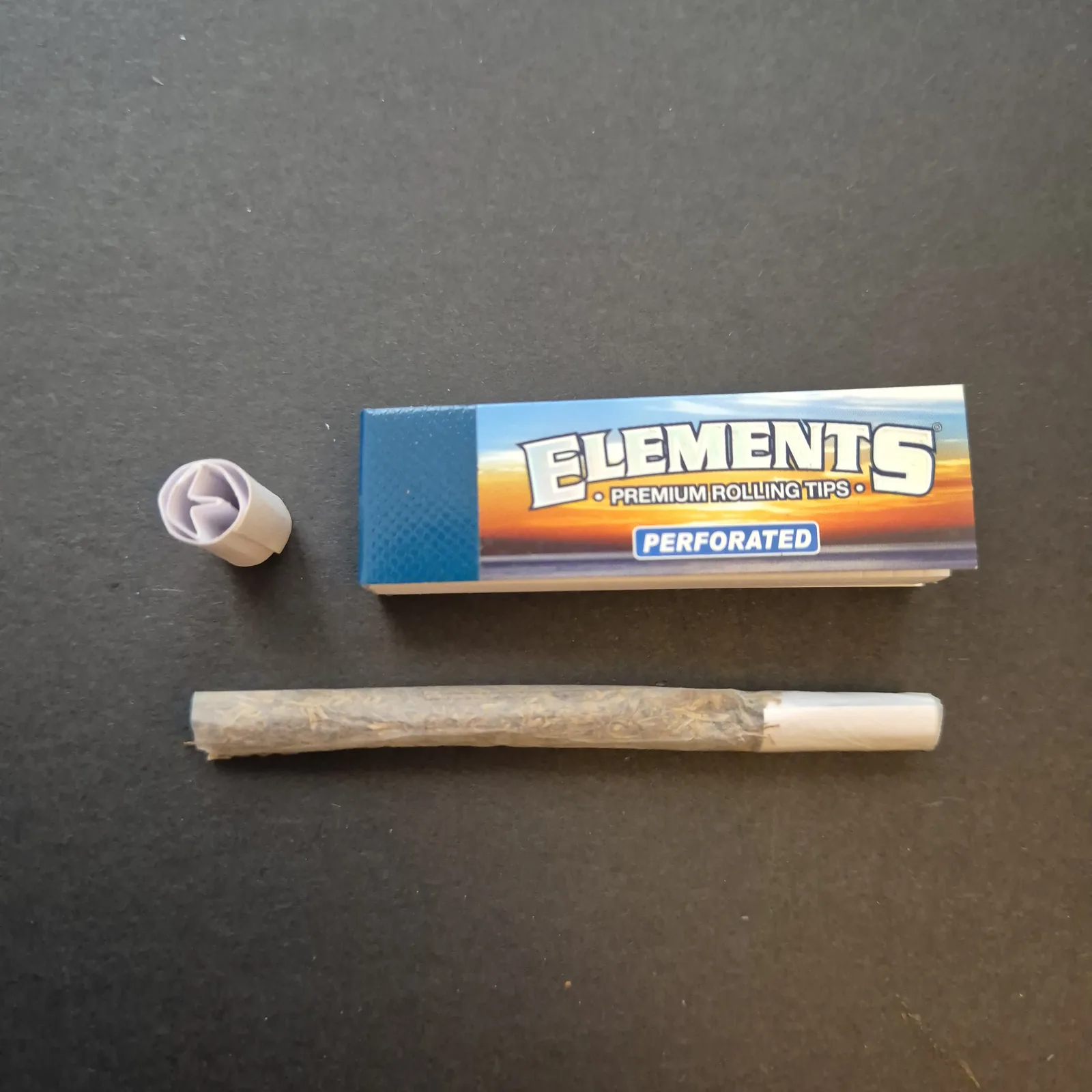 フィルターの代わりに紙のチップを入れた手巻き。横に巻いたチップとElements Rolling Tipsのパッケージ