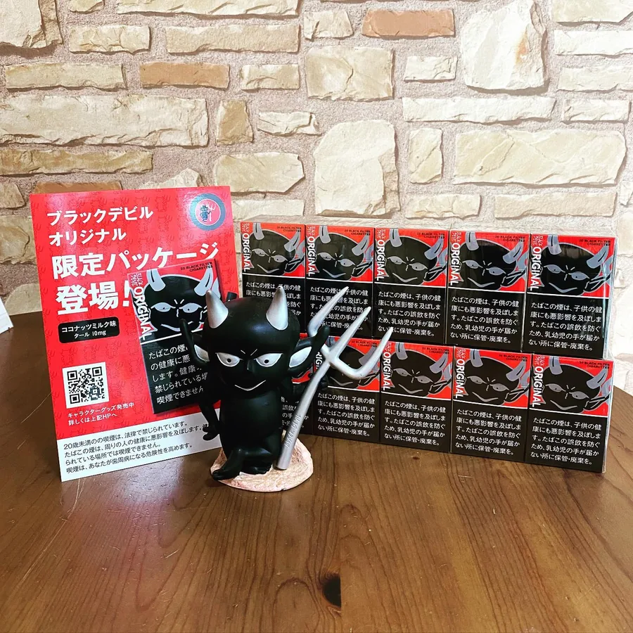 한정 패키지(ブラックデビル オリジナル 限定パッケージ)의 Black Devil Original 담배 — 코코넛 밀크 맛 에디션으로, Black Devil 피규어와 제조사의 안내 카드 뒤에 쌓여 있음 — Himawari Tobacco Shop, Tsuruga