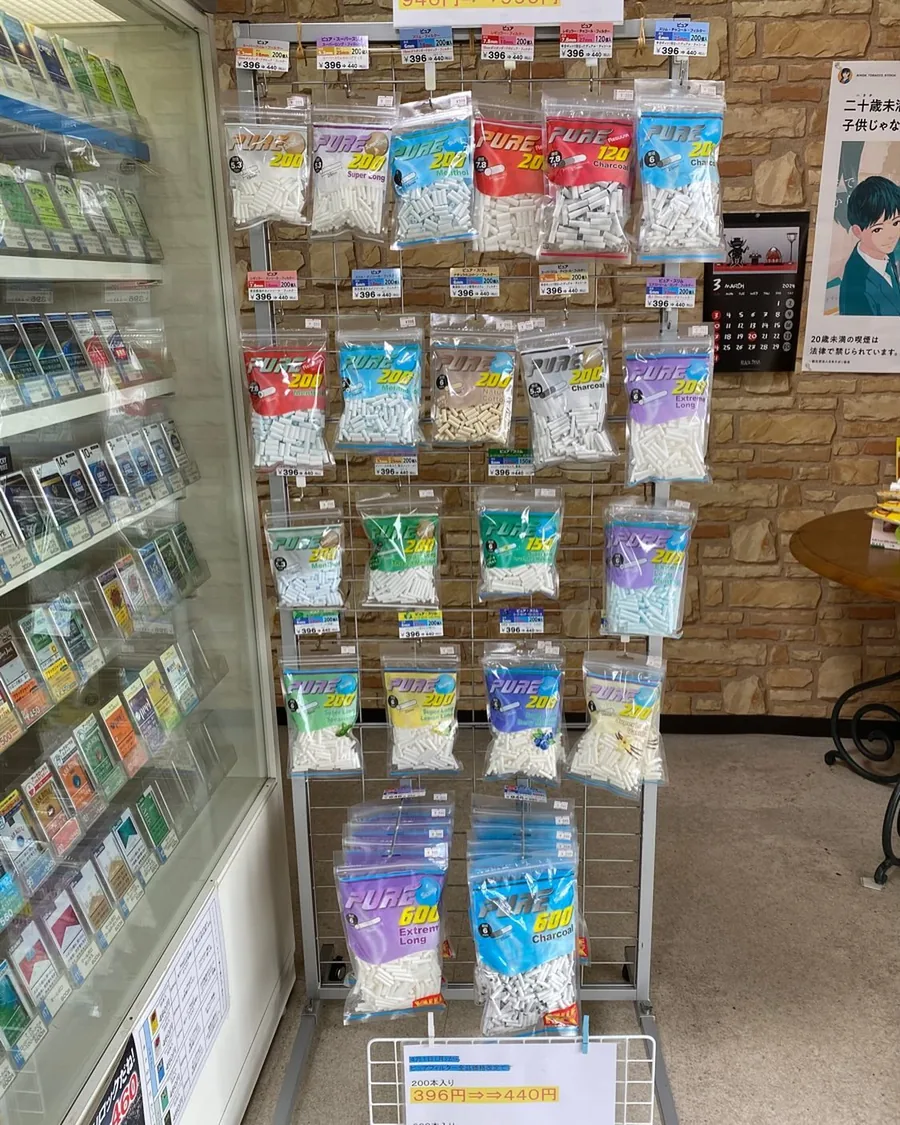다양한 길이와 맛의 PURE 롤링 필터 봉지가 걸린 랙, 그 옆에 유리 궐련 진열장 — Himawari Tobacco Shop, Tsuruga