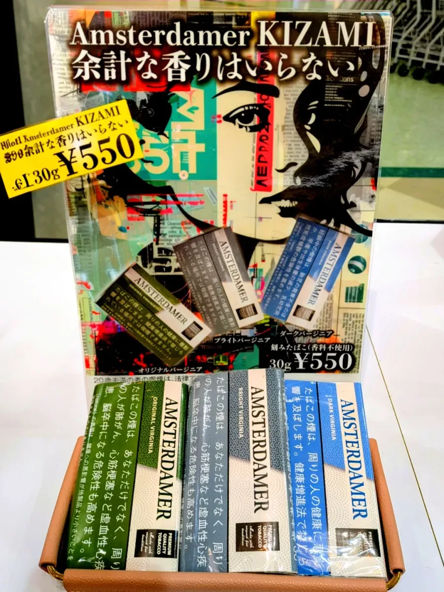 브랜드 포스터 앞 트레이에 놓인 Amsterdamer Kizami 각초 담배 진열 — Original Virginia, Bright Virginia, Dark Virginia, 모두 무향(香料不使用) — Icora Mall Tobacco Shop, Izumisano