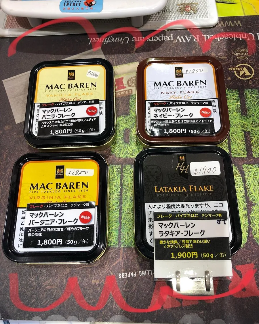 RAW 롤링 페이퍼 매트 위에 늘어놓은 Mac Baren 플레이크 파이프 담배 50g 캔 네 개 — Vanilla Flake, Navy Flake, Virginia Flake, HH Latakia Flake. 2018년 8월 — Shop Kita, Kawagoe